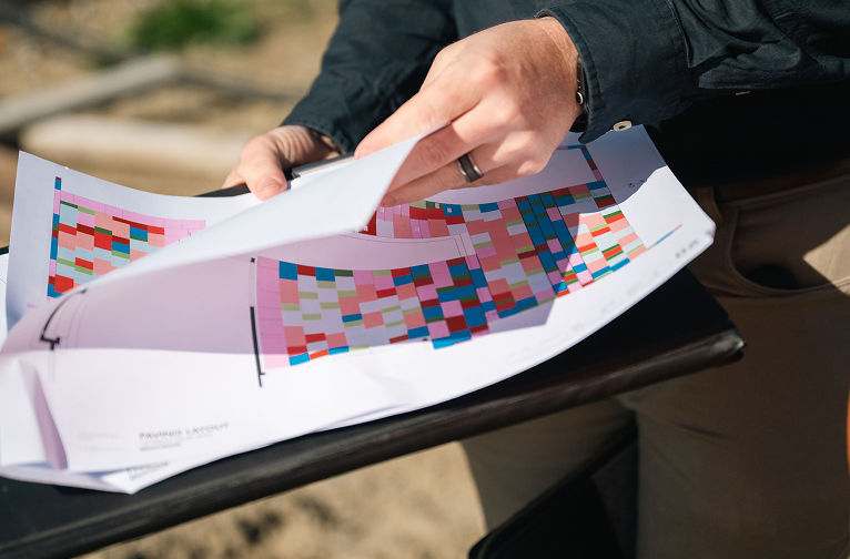 A close-up view of a Kūmānu staff member’s hands flipping through colourful planning documents outdoors.