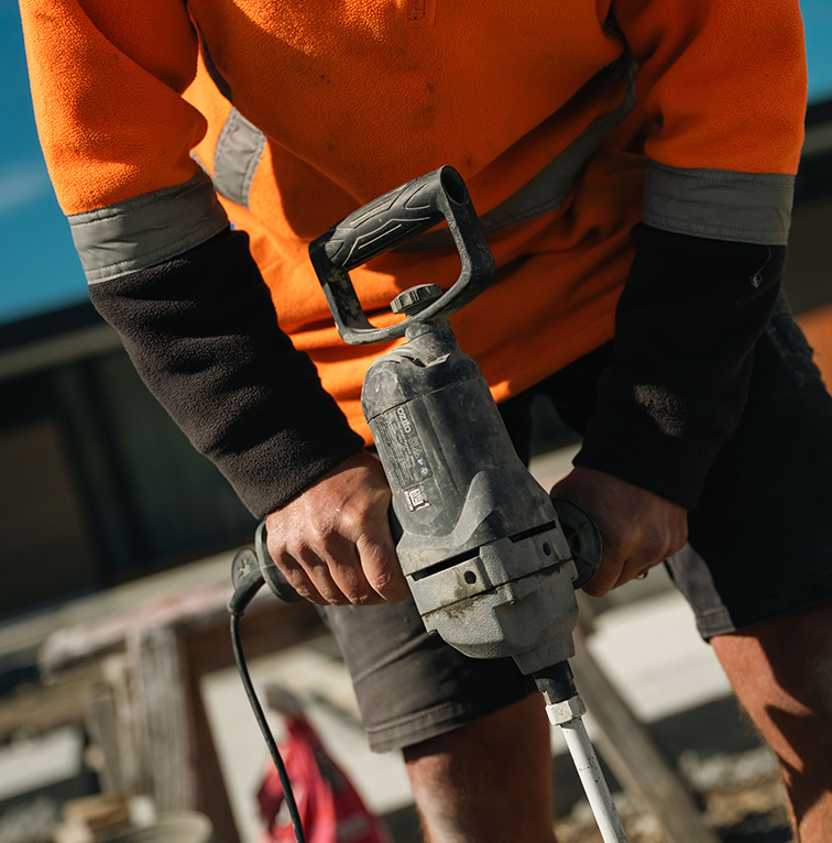 Close-up of a construction worker in a high-visibility jacket operating a handheld power tool on an outdoor worksite.