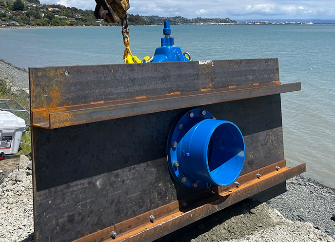 Blue water pipe opening mounted through a steel retaining wall beside a coastal shoreline