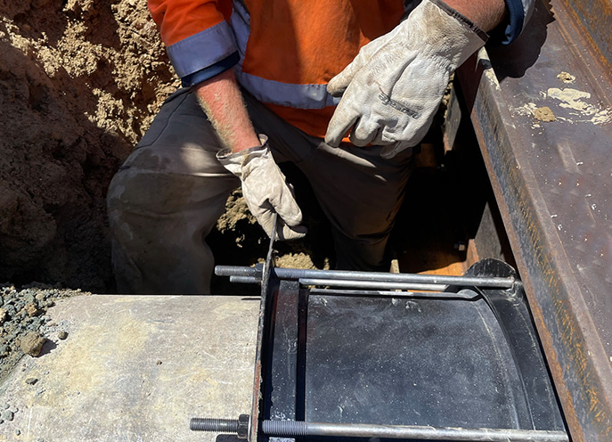 Close-up of workers’ hands and tools securing a black pipe connection inside a trench