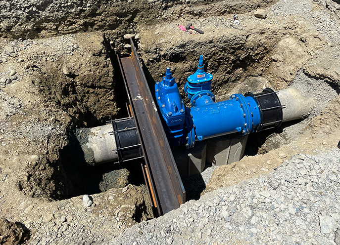 Installed blue water valve and pipe assembly set within a trench and supported by concrete blocks