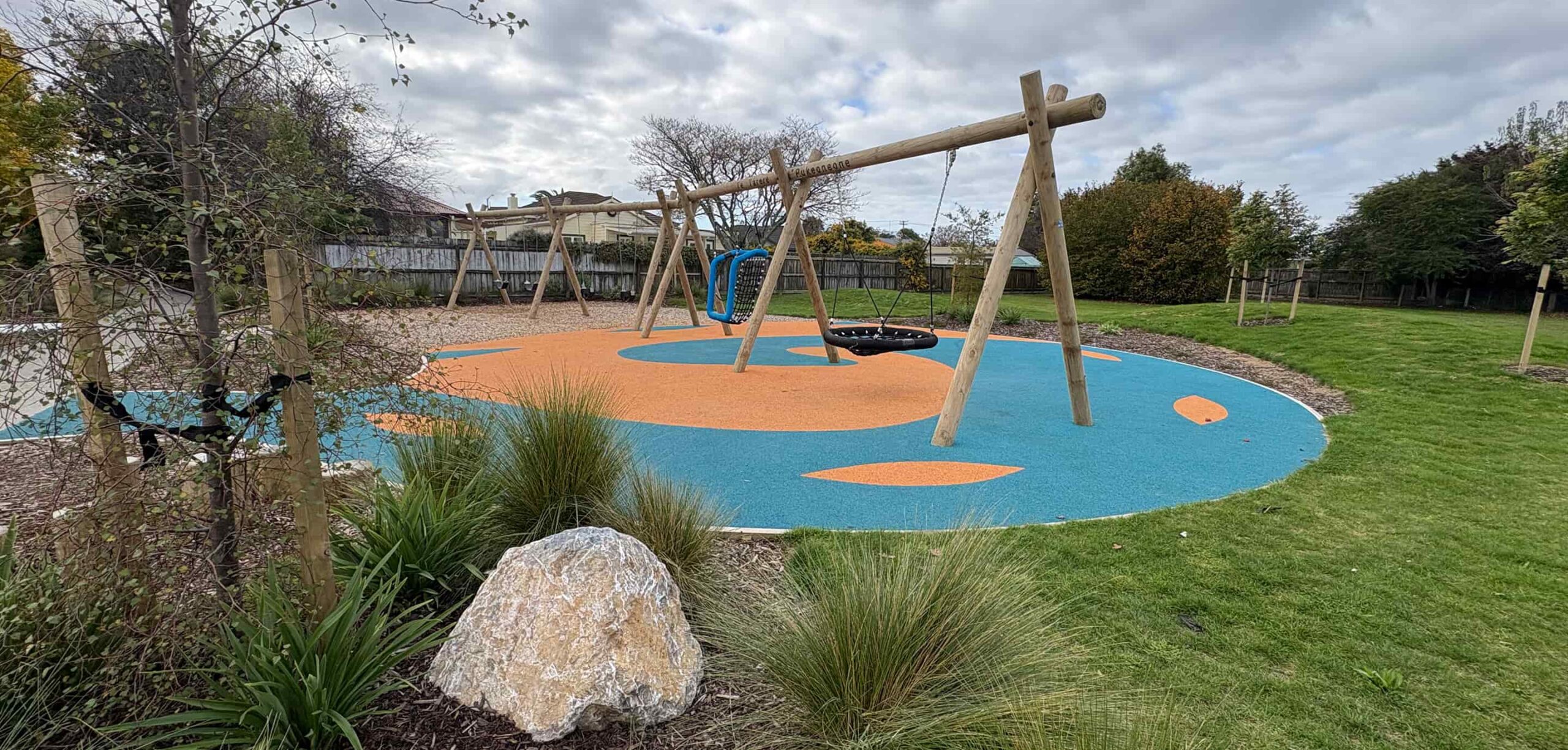 Wide view of the swing area at Decks Reserve with basket swing, rubber surfacing, and surrounding lawn