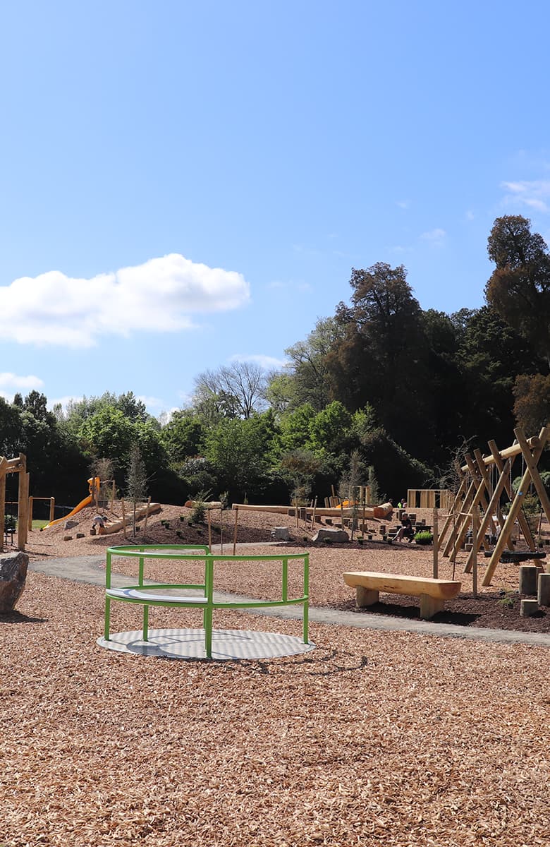 Wide view of the inclusive carousel and surrounding natural play landscape at Faulkner Bush Scenic Reserve