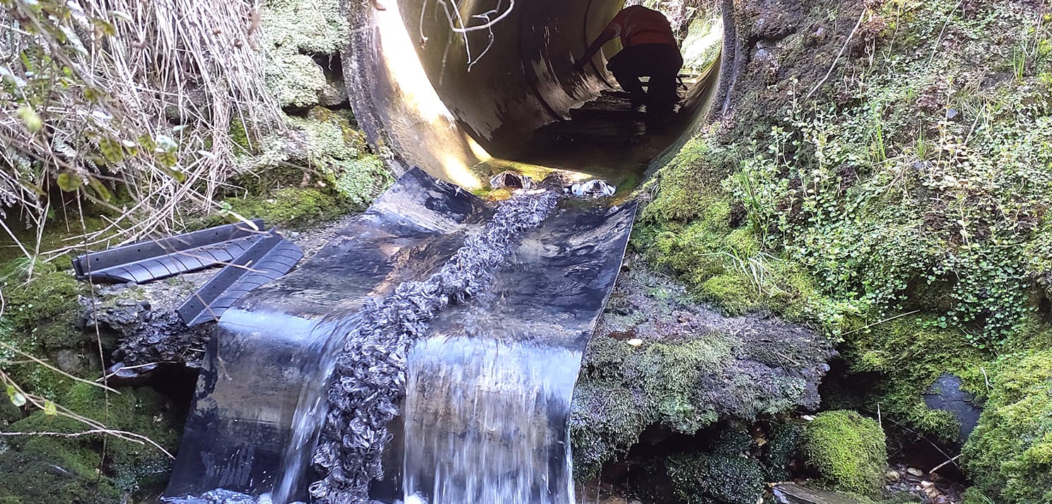 Fish passage remediation showing modified culvert outlet with water flowing over installed fish passage liner