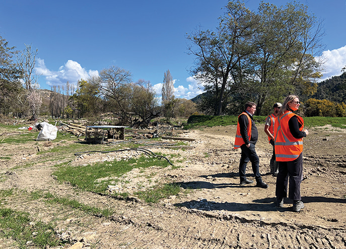Group of people in high-visibility vests standing on a cleared riverbed during a flood recovery site inspection