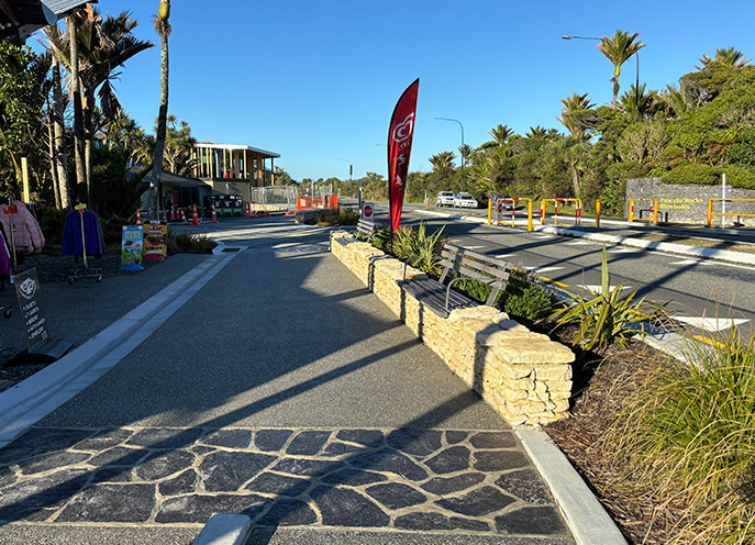 Roadside pedestrian path with stone walls, benches, and landscaped planting near the visitor centre