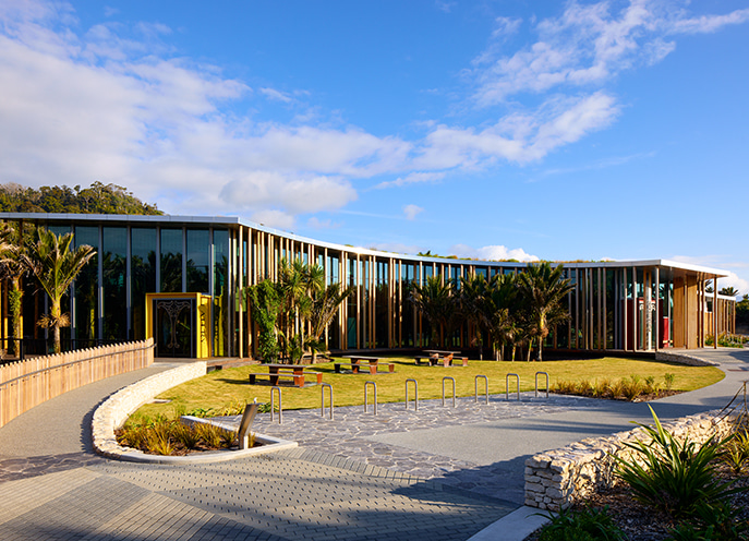 Front view of the visitor centre with timber vertical fins, glass façade, lawn, and outdoor seating