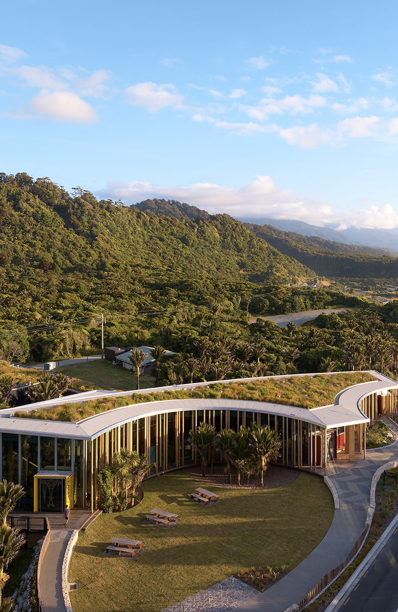 Portrait aerial view of the visitor centre building with surrounding road, coastal landscape, and forested hills