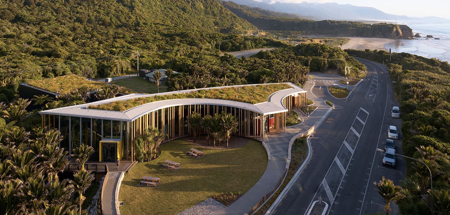 Aerial view of the visitor centre building with surrounding road, coastal landscape, and forested hills