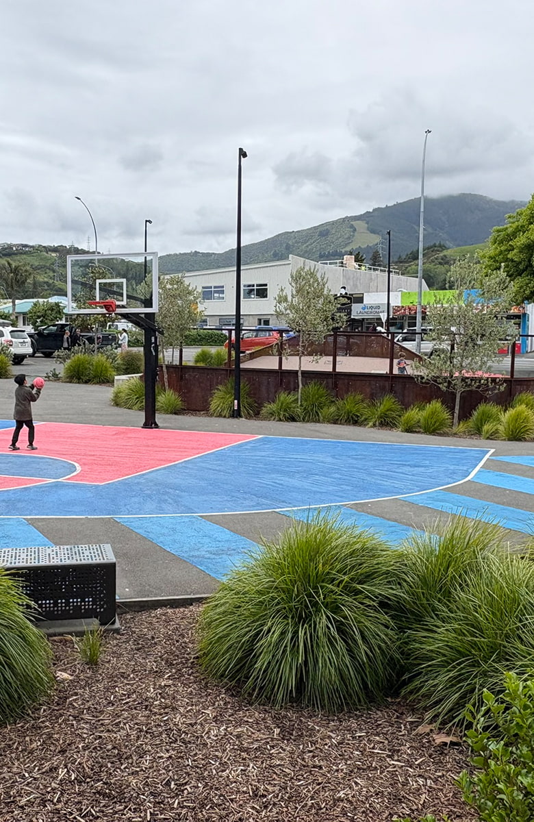 Outdoor basketball court with blue and red surfacing next to the skate park at Stoke Youth Park