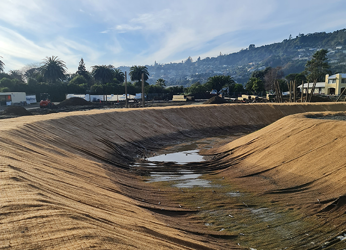 Earthworks forming a contoured stormwater basin at Te Pā Harakeke with surrounding trees and hillside housing