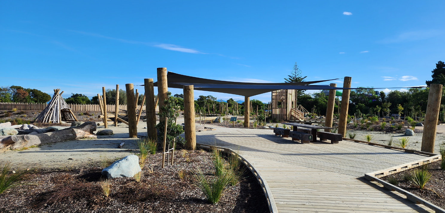 Curved timber boardwalk with shade sail and seating within the Te Pā Harakeke community playspace