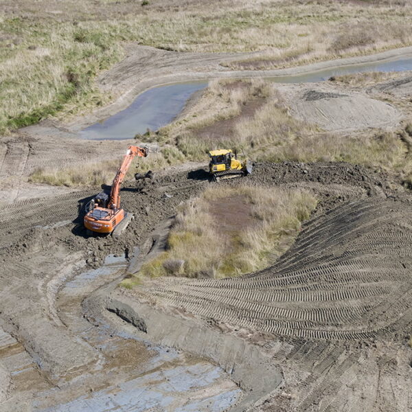 Aerial view of wetland earthworks with an excavator and bulldozer shaping channels and contours in an open grassland area