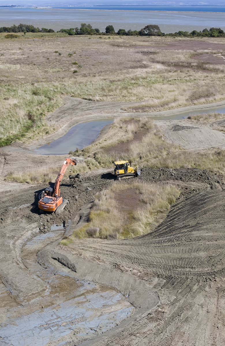 Aerial view of an excavator and bulldozer working beside newly formed wetland channels with standing water