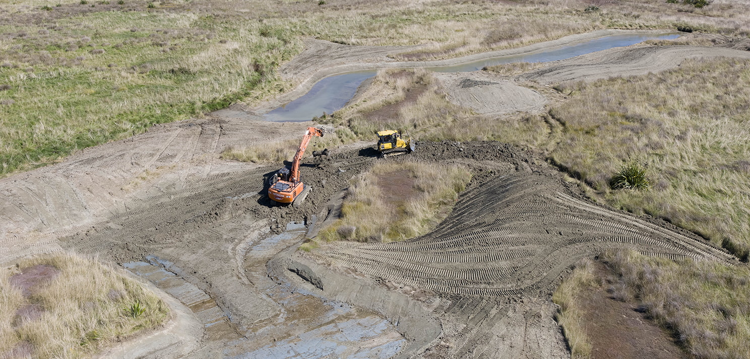 Aerial view of wetland earthworks with an excavator and bulldozer shaping channels and contours in an open grassland area
