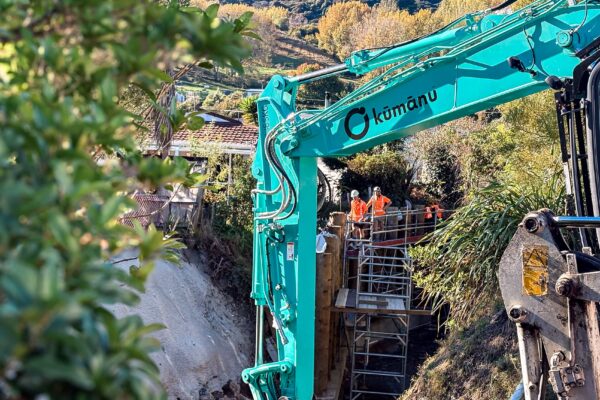Kūmānu’s site team coordinates crane-lifted materials for waterway erosion control works in a tight residential stream environment.